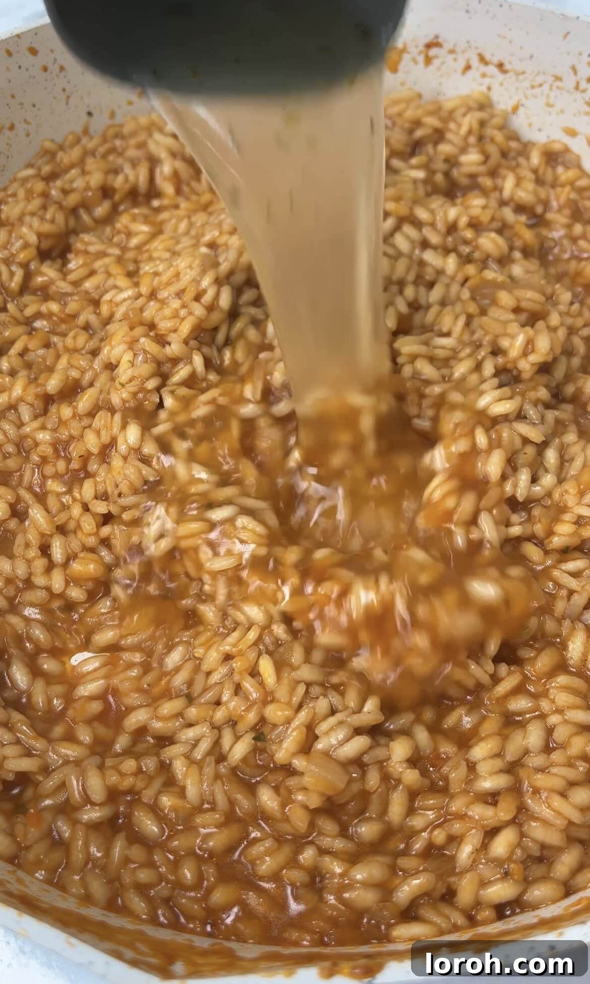 Continued gradual addition of hot stock to the risotto, stirring constantly.