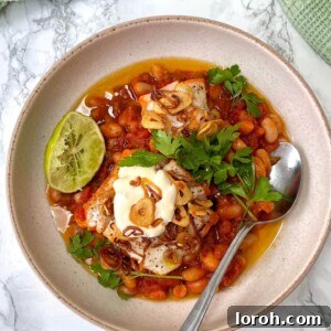 One Pan Poached Fish with Brothy Tomato Beans and Saffron Aioli, garnished with crispy garlic and frazzled shallots