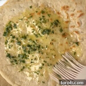 Freshly baked garlic naan being brushed with garlic butter, showcasing a fluffy texture and charred spots.