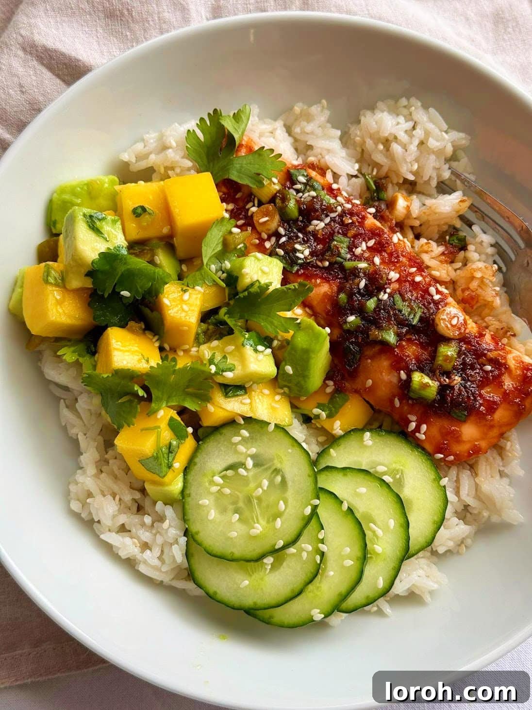 Delicious and healthy Teriyaki Salmon Bowl with mango avocado salsa and rice, garnished with spring onions and sesame seeds.