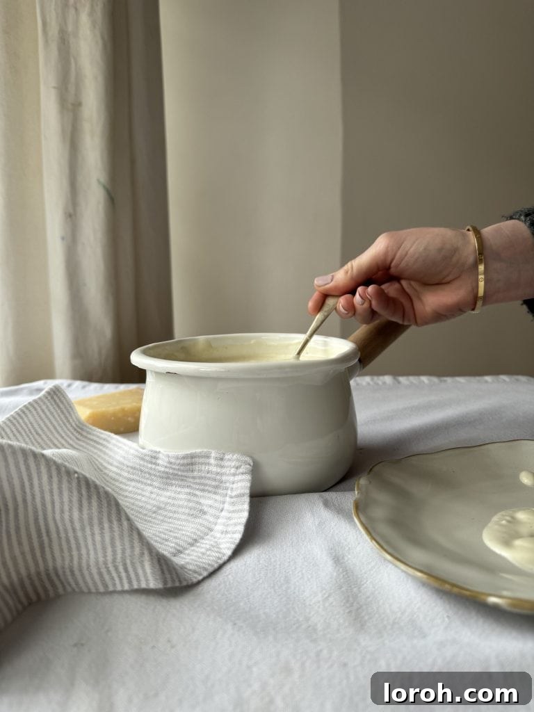 Woman holding a spoon in a saucepan of creamy white sauce, demonstrating perfect texture.