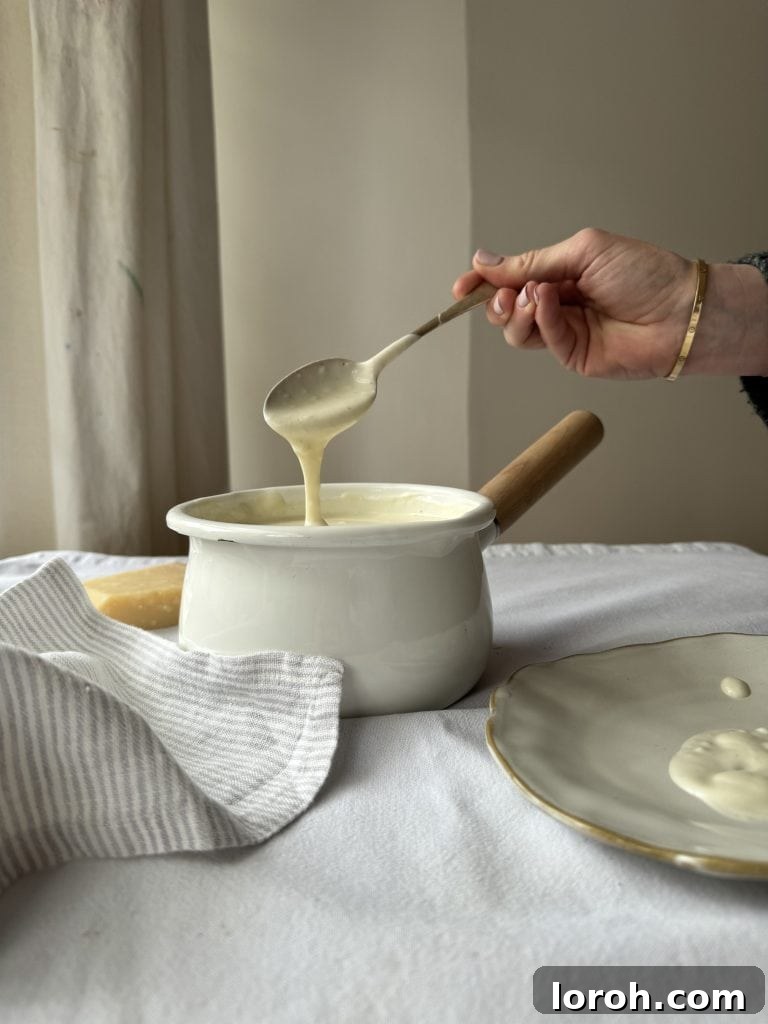 Woman gently stirring a saucepan of white sauce with a spoon, highlighting its smooth consistency.