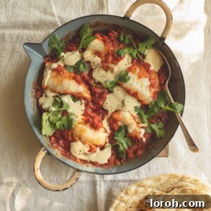 A pan of tomato sauce with white fish, tahini drizzle and coriander leaves scattered