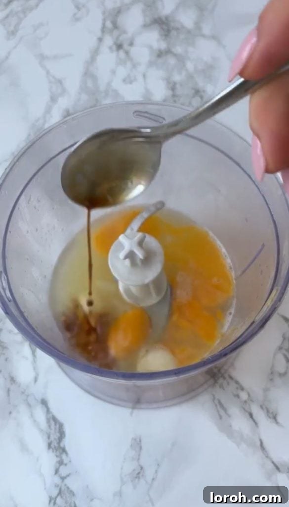 Adding Worcestershire sauce to a blender containing egg yolks, lemon juice, and garlic cloves