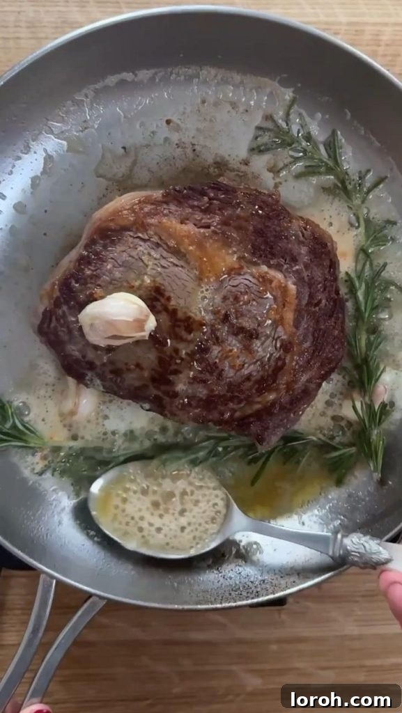 A person basting a sizzling rib eye steak in a cast iron pan with rosemary-garlic butter. The steak has a perfect sear, and the rich butter is spooned over it, infusing it with aromatic flavors and keeping it moist.