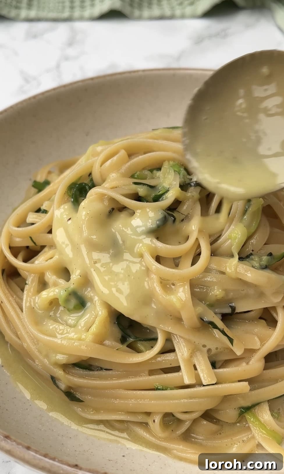 Lemony Courgette Carbonara: Freshly poured creamy sauce over pasta with zucchini ribbons and basil garnish.