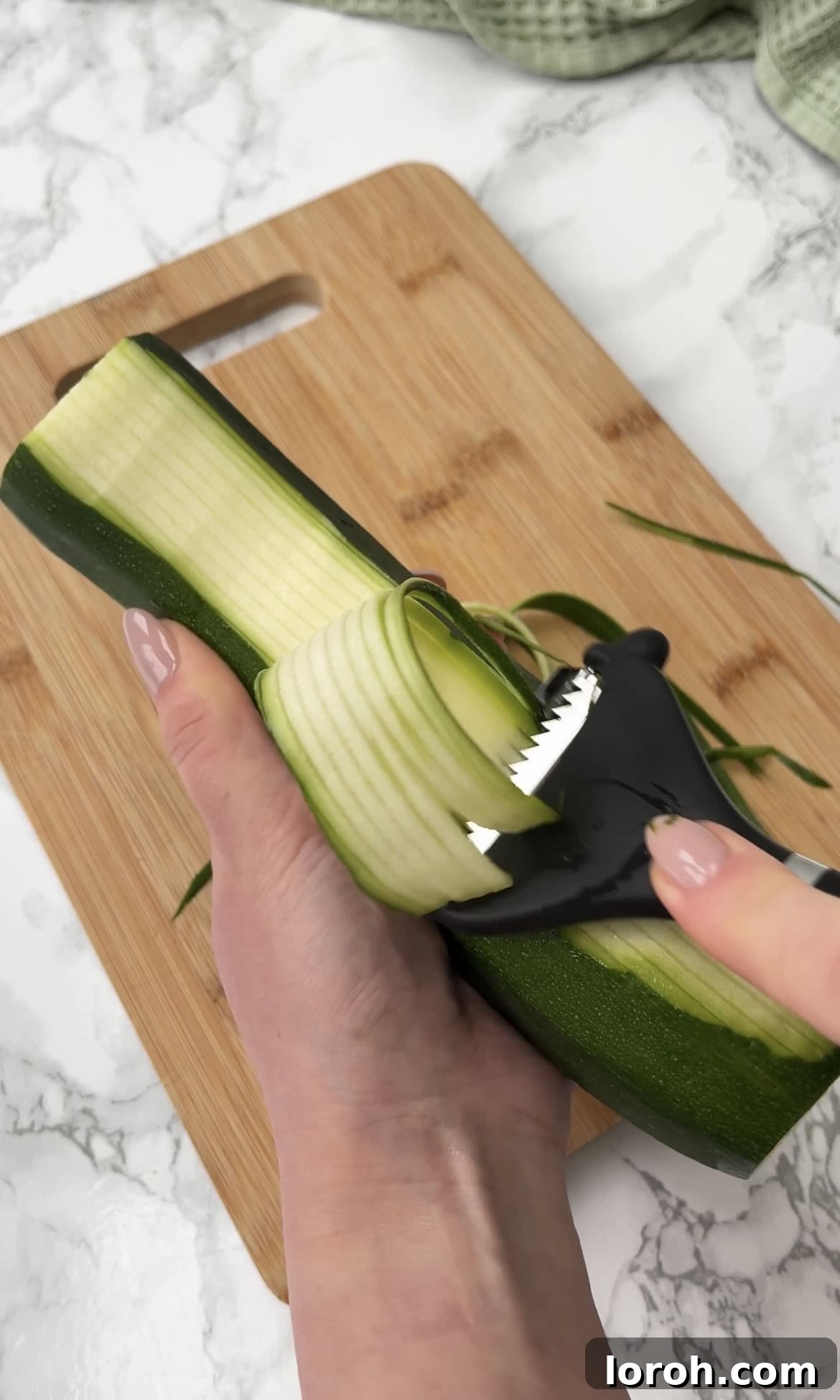 Using a julienne peeler to slice a courgette into thin noodles for pasta.