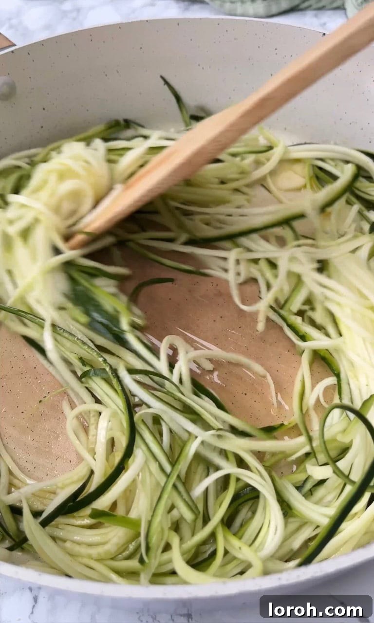 Frying julienned courgettes in a pan with garlic and olive oil.