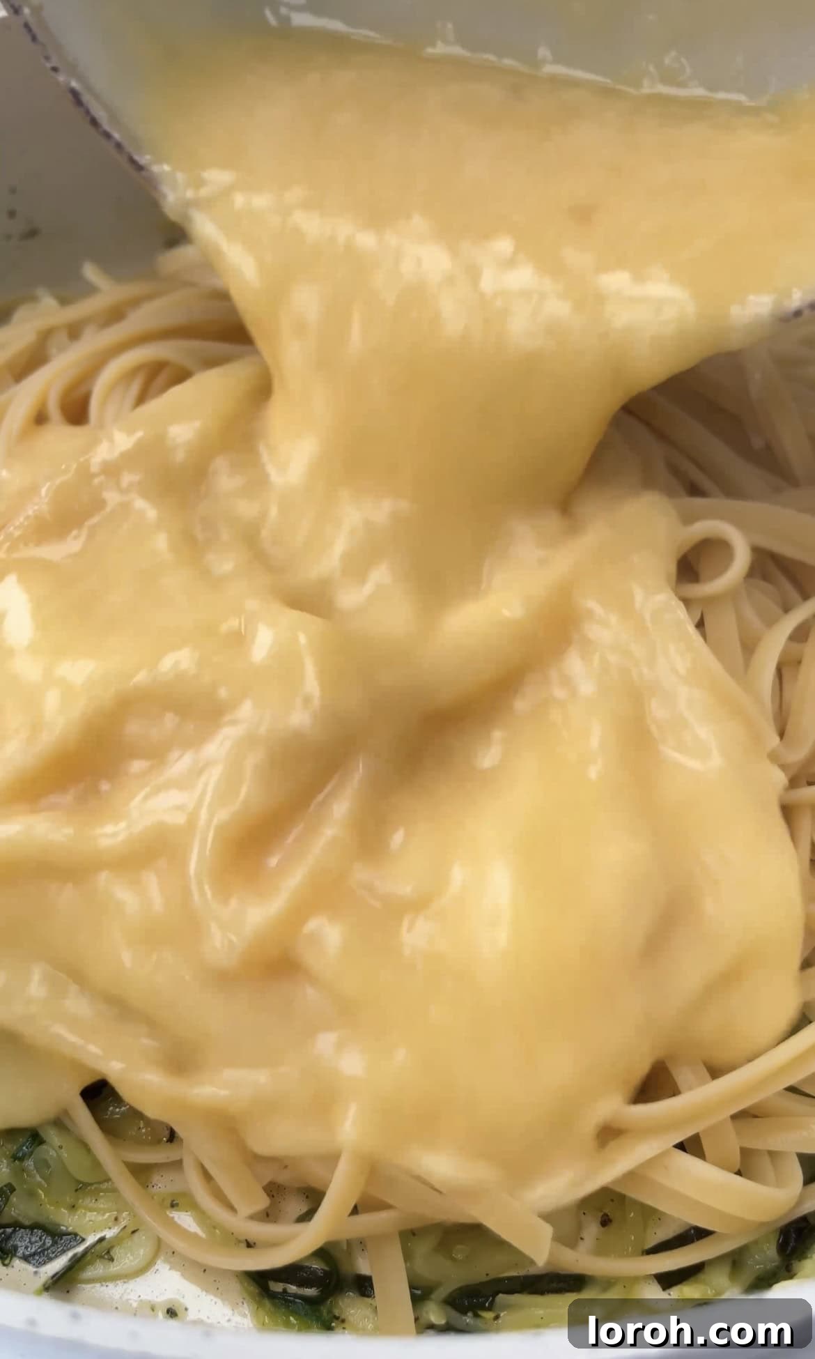 Pouring the tempered egg and cheese mixture over cooked pasta and courgettes in a pan.