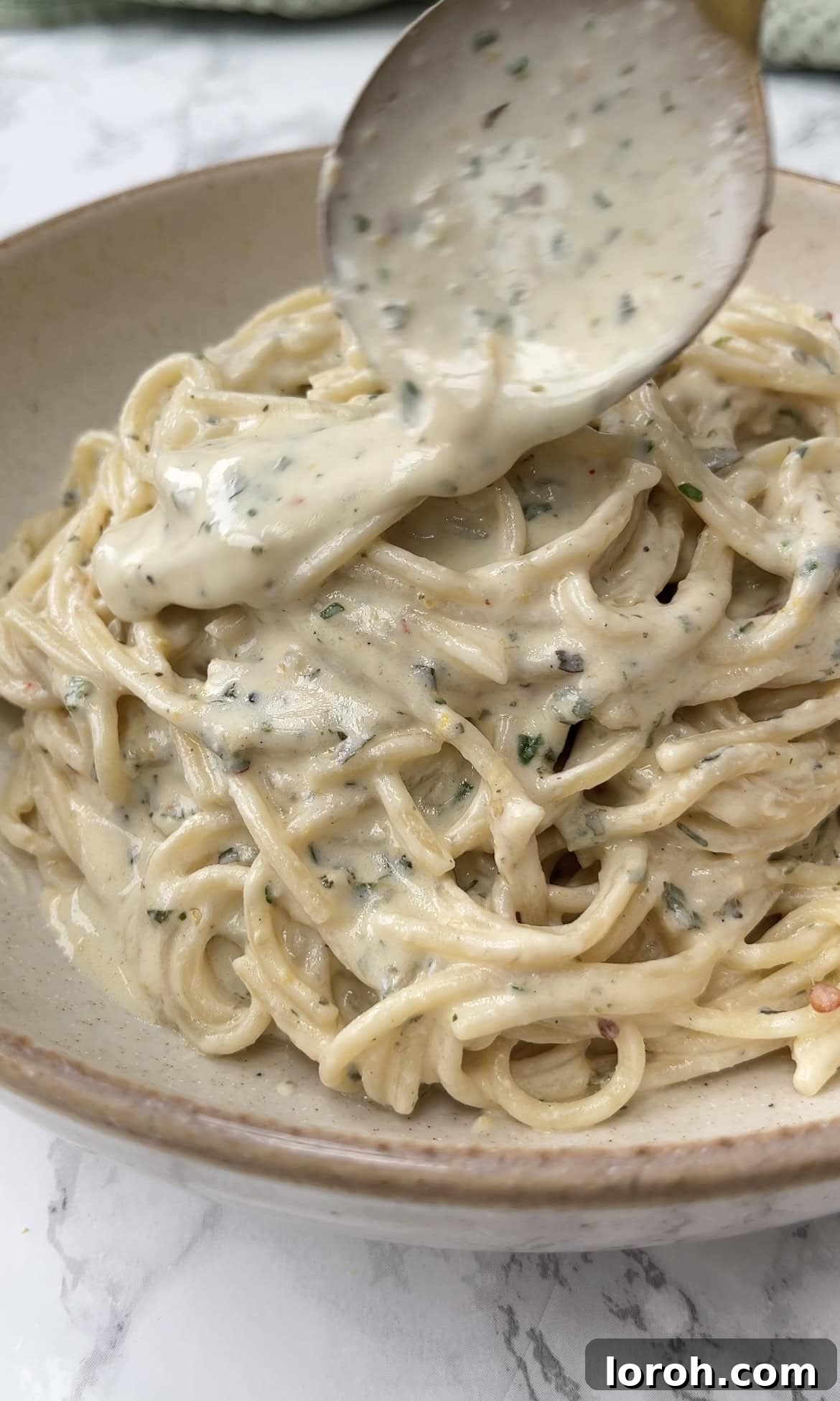 Creamy Lemon Artichoke Boursin Pasta Bake 3 A close-up of a serving spoon scooping the rich, creamy Boursin pasta sauce over spaghetti in a baking dish.