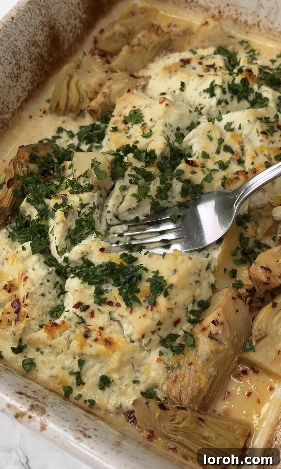 Creamy Lemon Artichoke Boursin Pasta Bake 7 A fork mashing baked garlic cloves into the creamy Boursin and artichoke sauce in a baking dish.