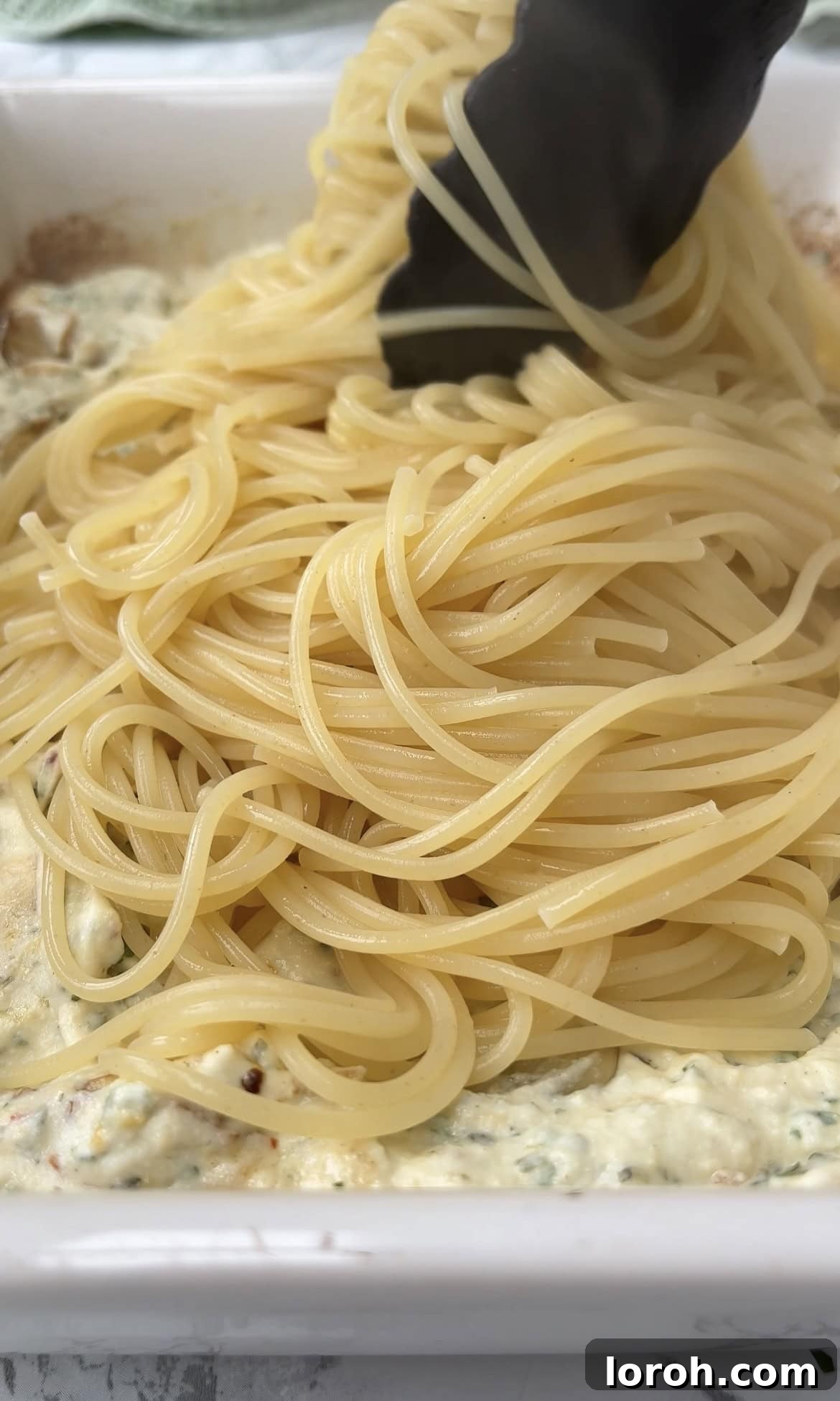 Creamy Lemon Artichoke Boursin Pasta Bake 8 Cooked spaghetti being added to the baked Boursin and artichoke sauce in a large baking dish.