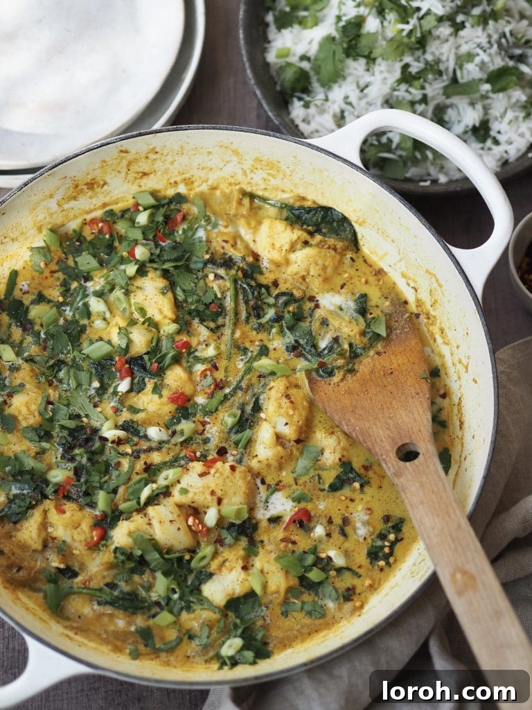 White shallow casserole dish with a fish and spinach curry next to serving bowls and a bowl of herbed rice.