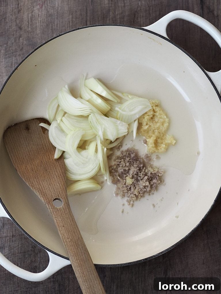 Sliced onions, ginger, garlic and spices in a shallow casserole dish.
