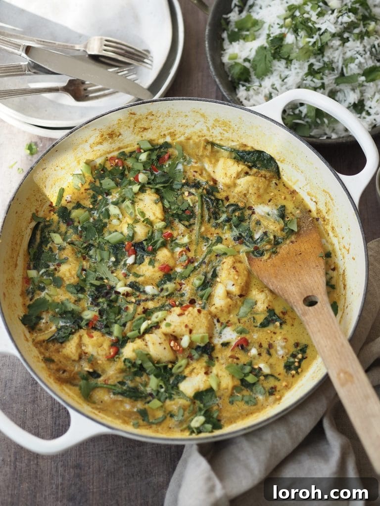 A cod and coconut curry with wilded spinach and red chilli in a white casserole dish.
