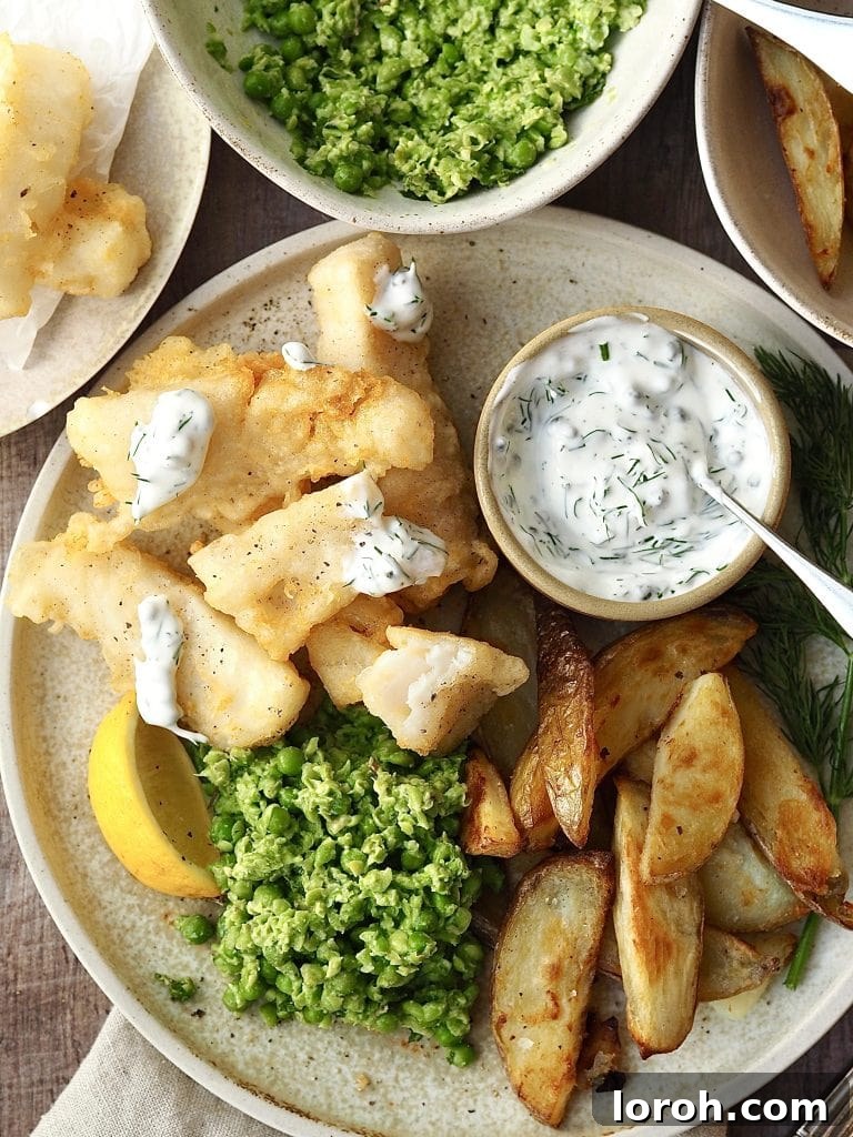 Golden Crispy Cod with Tartar Zing 2 Fish goujons on a plate with potato wedges, lemon and peas drizzled with homemade tartare sauce.