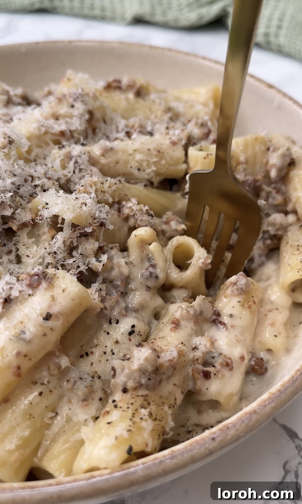 Fork twirling perfectly coated rigatoni with creamy sausage sauce, highlighting the texture and richness of the dish in a rustic bowl.