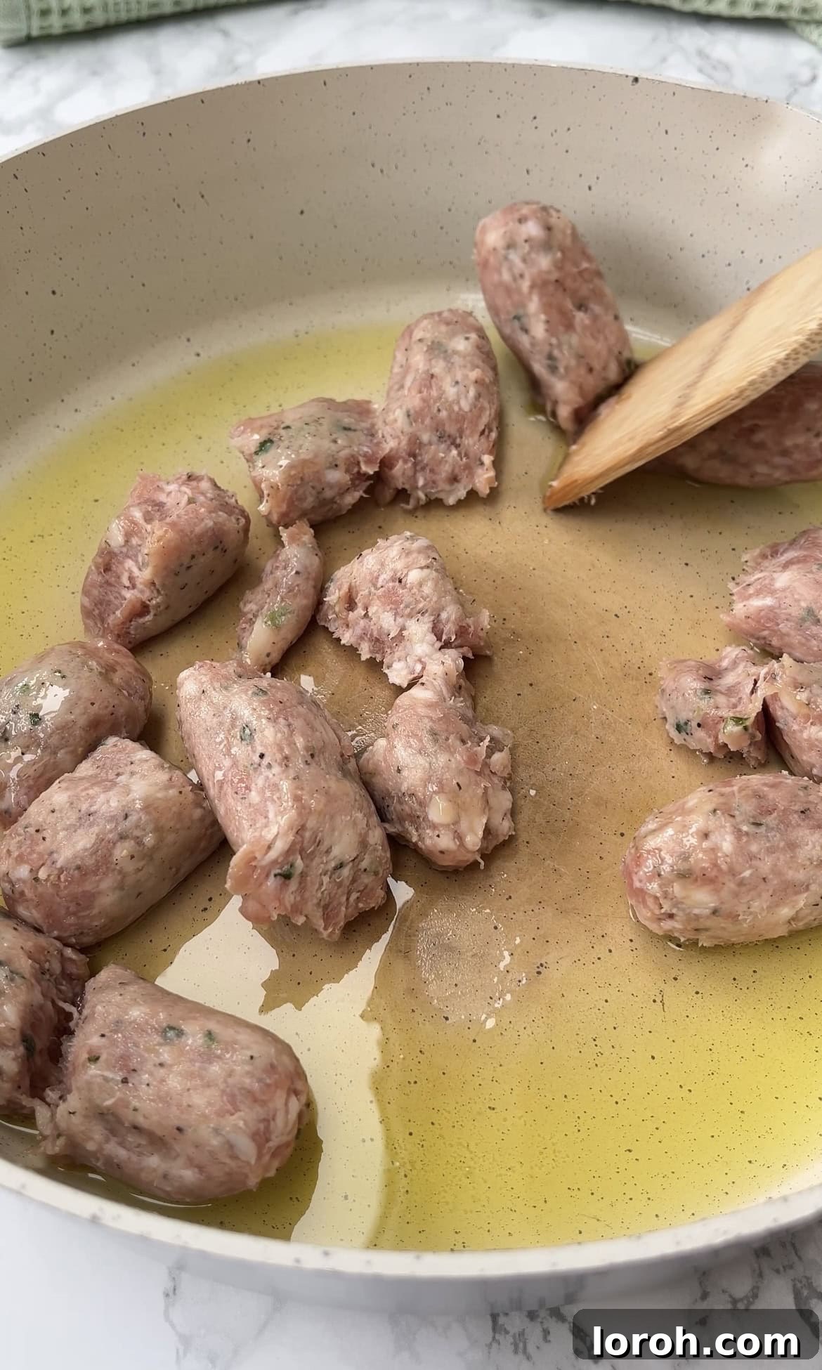 Sausage meat browning and crumbling in a hot pan with olive oil, developing a delicious golden crust.
