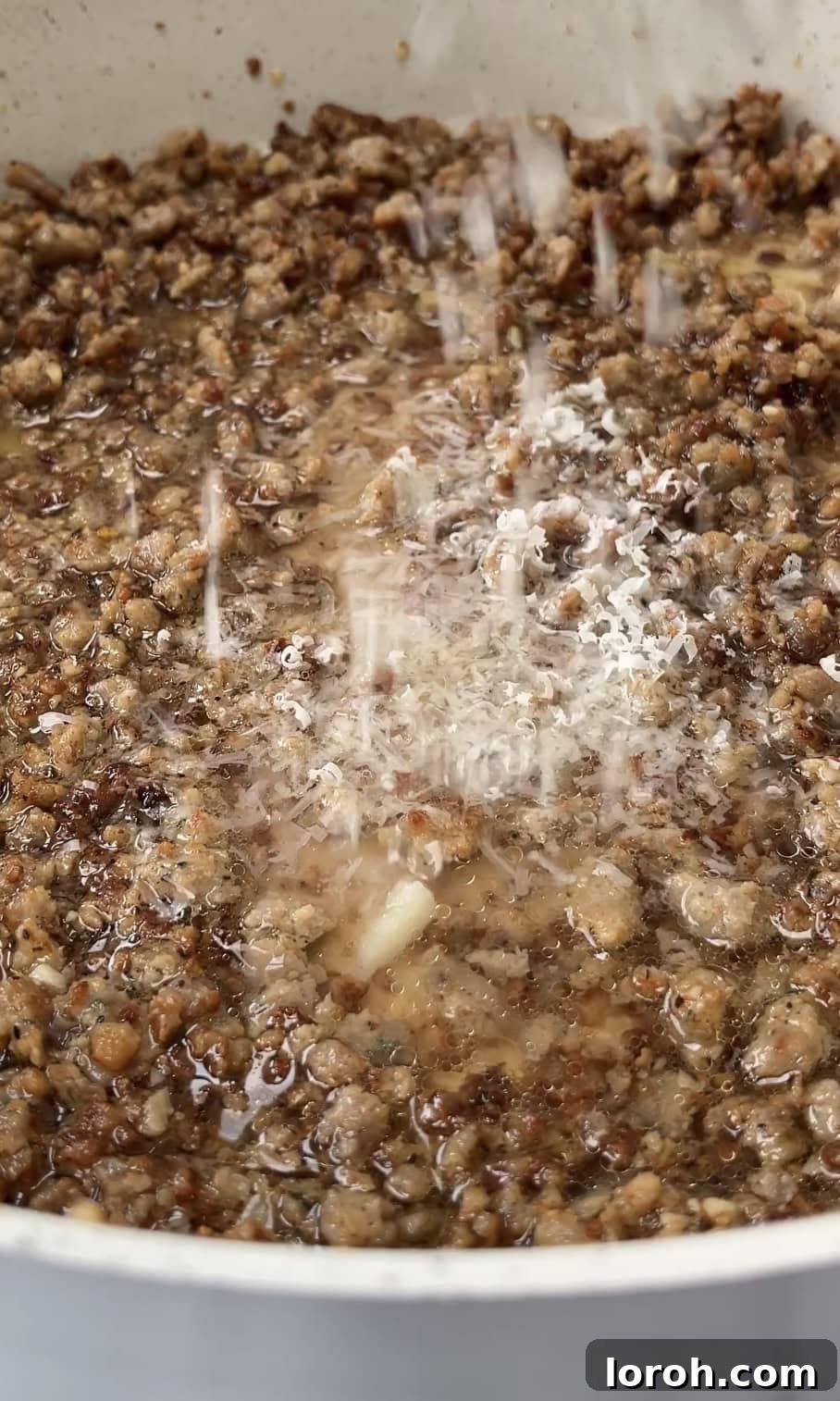 Grated Pecorino Romano cheese being stirred into the simmering creamy sausage sauce, melting beautifully.