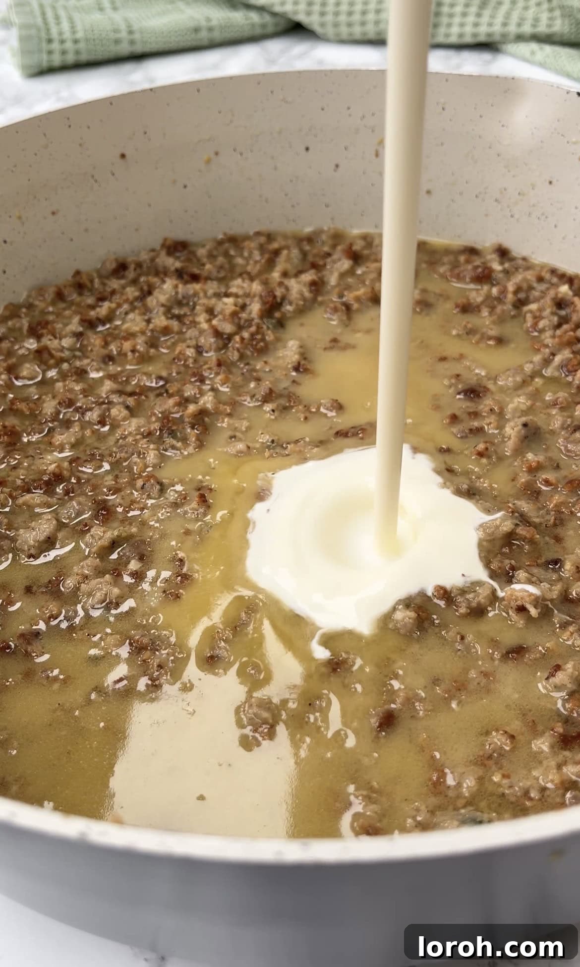 Single cream being poured into the rich sausage and cheese sauce in a large pan, making it irresistibly smooth and luscious.
