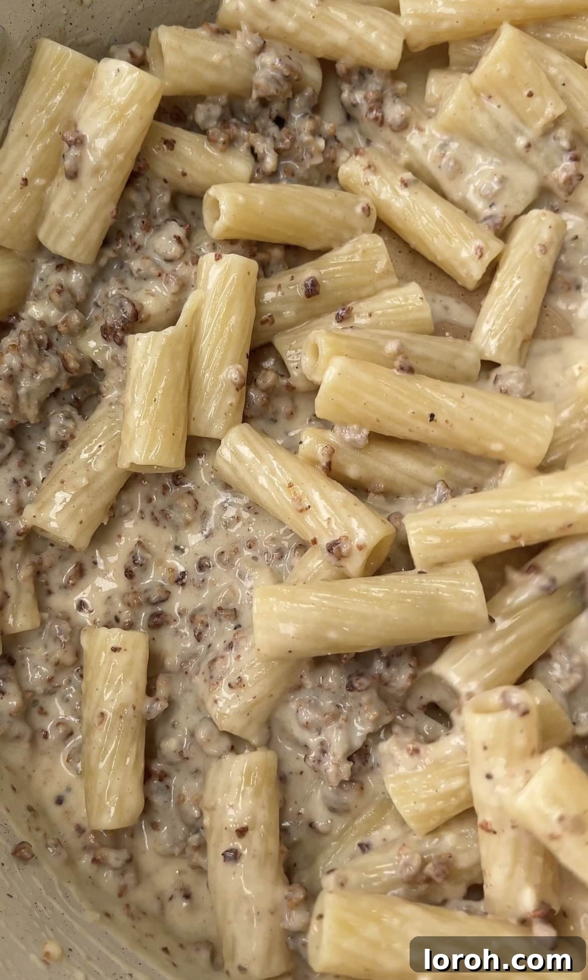 Creamy sausage pasta being tossed vigorously together in a large pan, ensuring every piece is coated with the rich sauce.