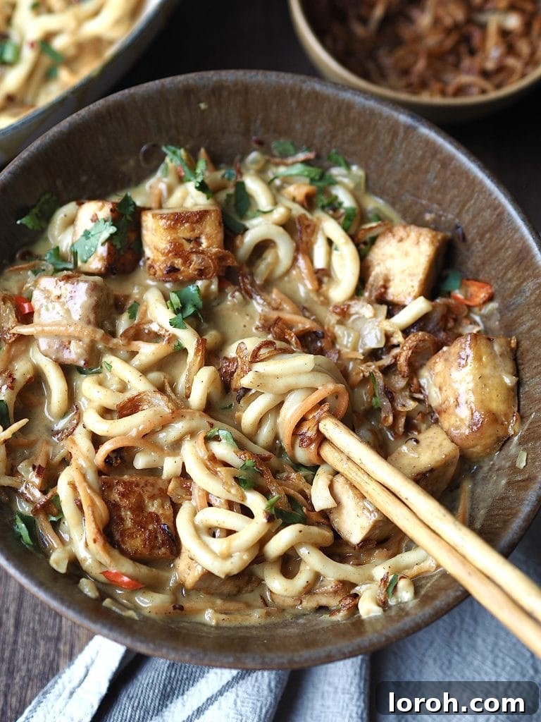 A bowl of curry udon soup being stirred withy chopsticks.