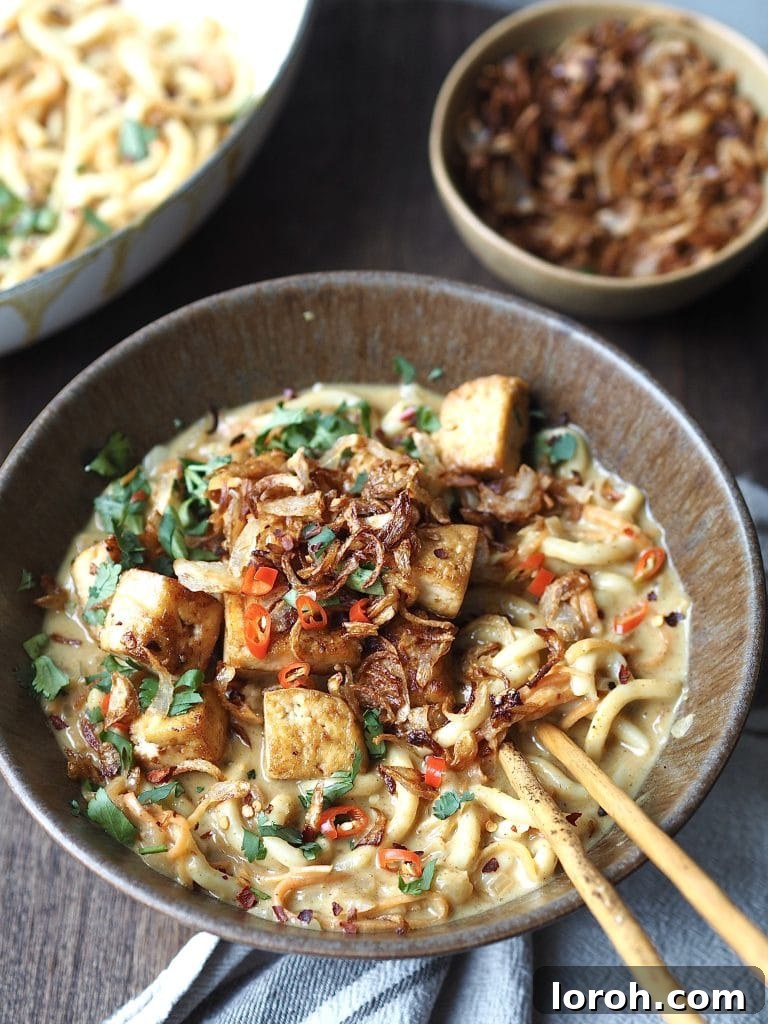 A close up of a bowl of curry udon noodles topped with crispy tofu cubes, fried shallots and sliced chilli.