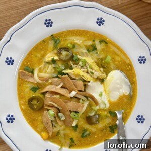 Bowl of chicken chilli con carne in a white bowl with blue flowers and a spoon of sour cream