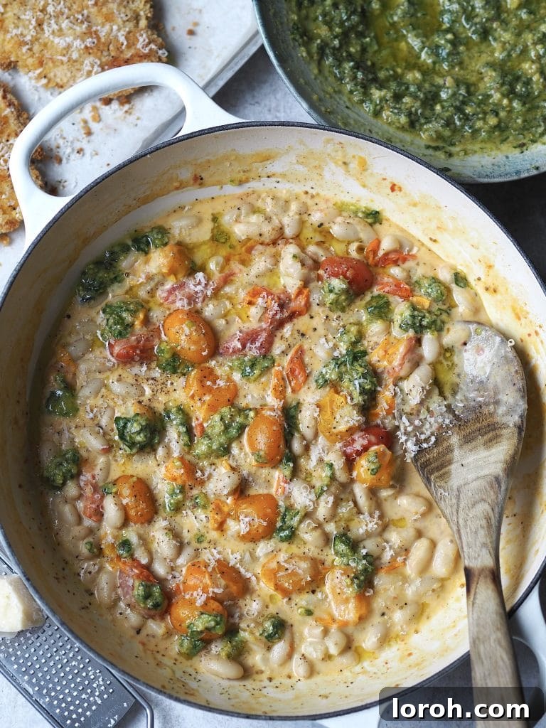 Crispy Chicken with Mediterranean White Bean Salad 3 Close up of a white shallow casserole with creamy beans and cherry tomatoes drizzled with pesto.