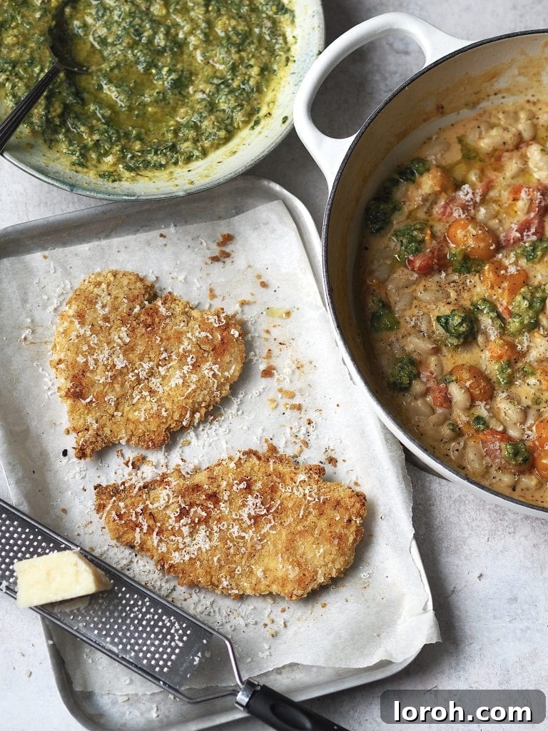 Crispy Chicken with Mediterranean White Bean Salad 10 Tray of cooked crispy chicken cutlets topped with grated parmesan next to dishes of creamy tomato beans and homemade basil pesto.