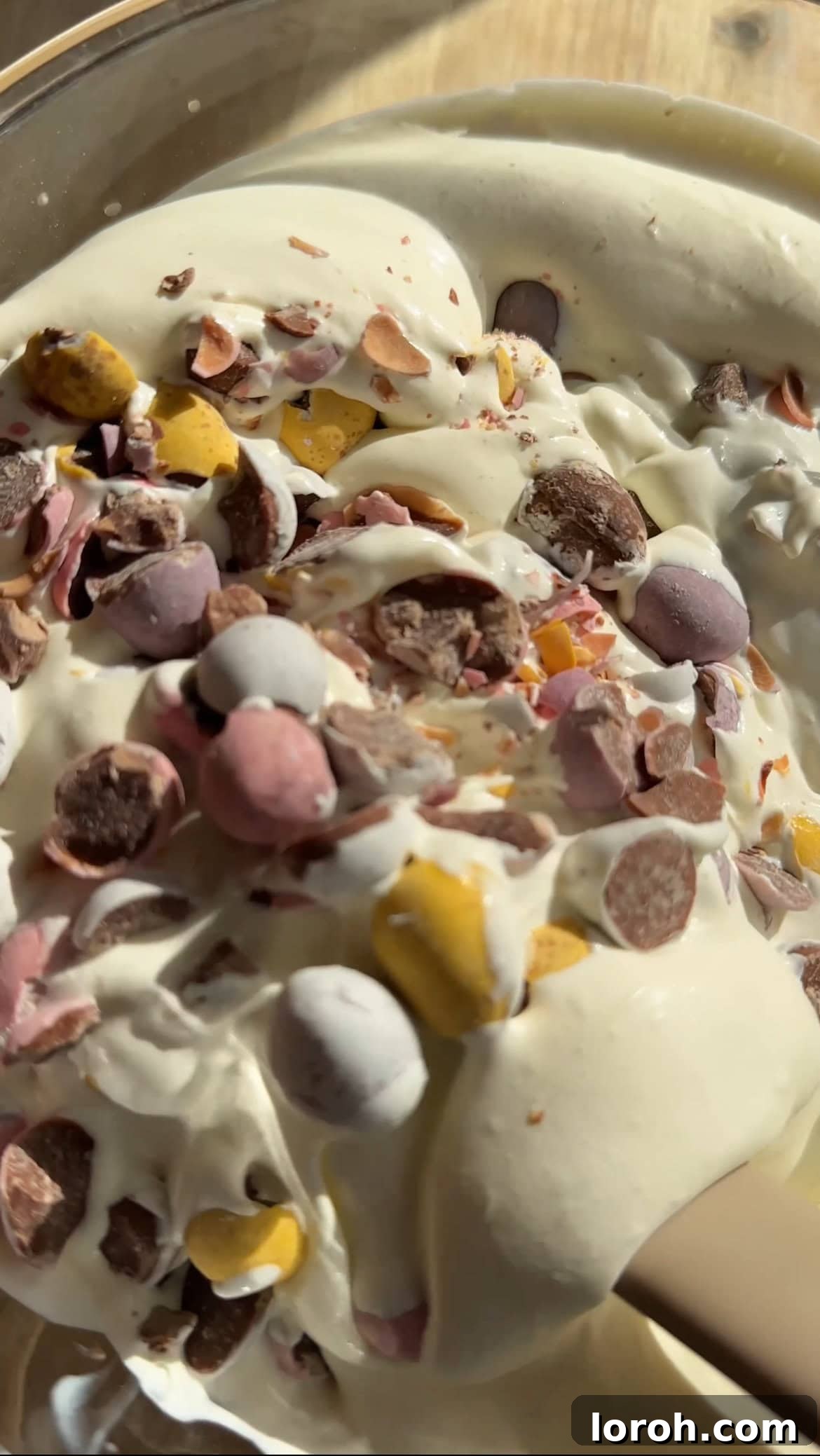 Gently folding crushed Mini Eggs into the thick cheesecake mixture with a spatula, ensuring even distribution of the chocolate pieces.