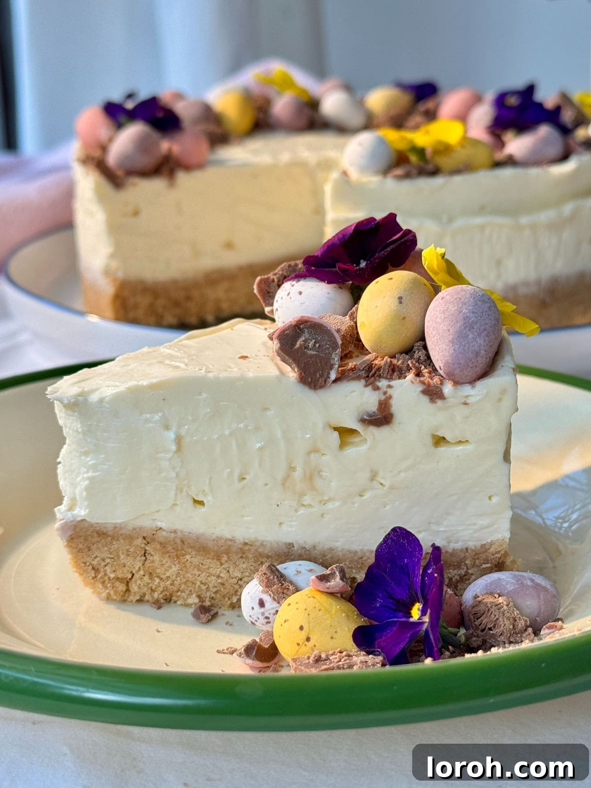 A perfectly sliced piece of Mini Egg Cheesecake, showcasing its creamy texture, embedded mini eggs, and crisp biscuit base.
