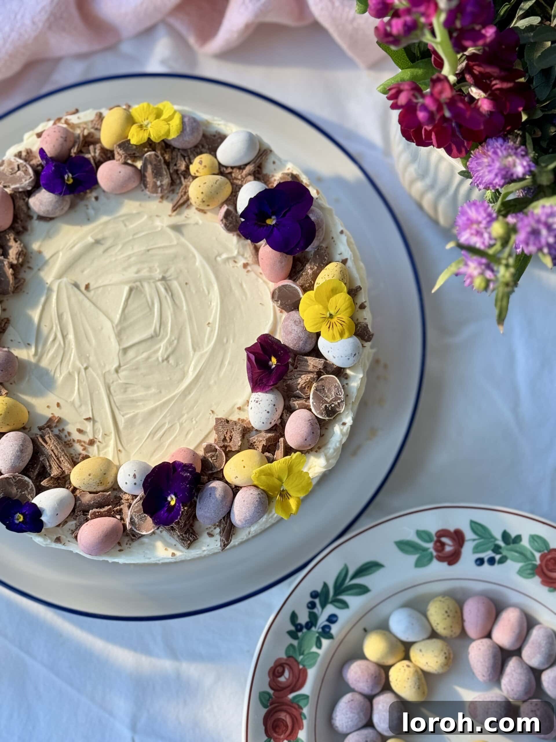 A close-up of a Mini Egg Cheesecake adorned with colorful Mini Eggs and delicate edible flowers, perfect for Easter.