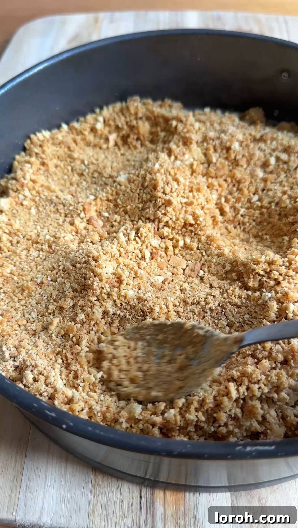 Smoothly pressing biscuit crumbs into the base of a springform tin, creating a compact and even layer.