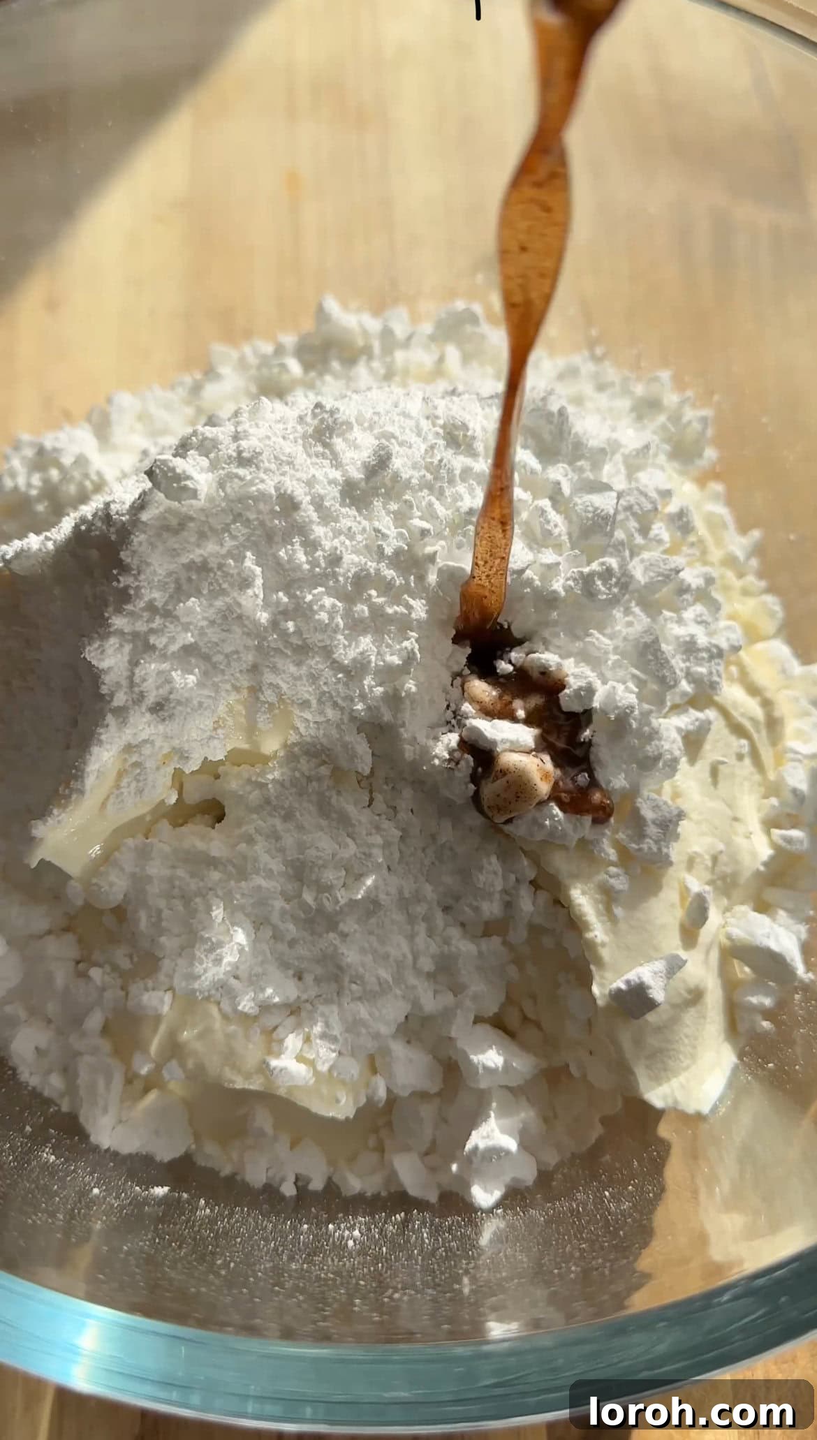 Adding vanilla extract to a bowl of cream cheese and icing sugar, preparing the cheesecake mixture.
