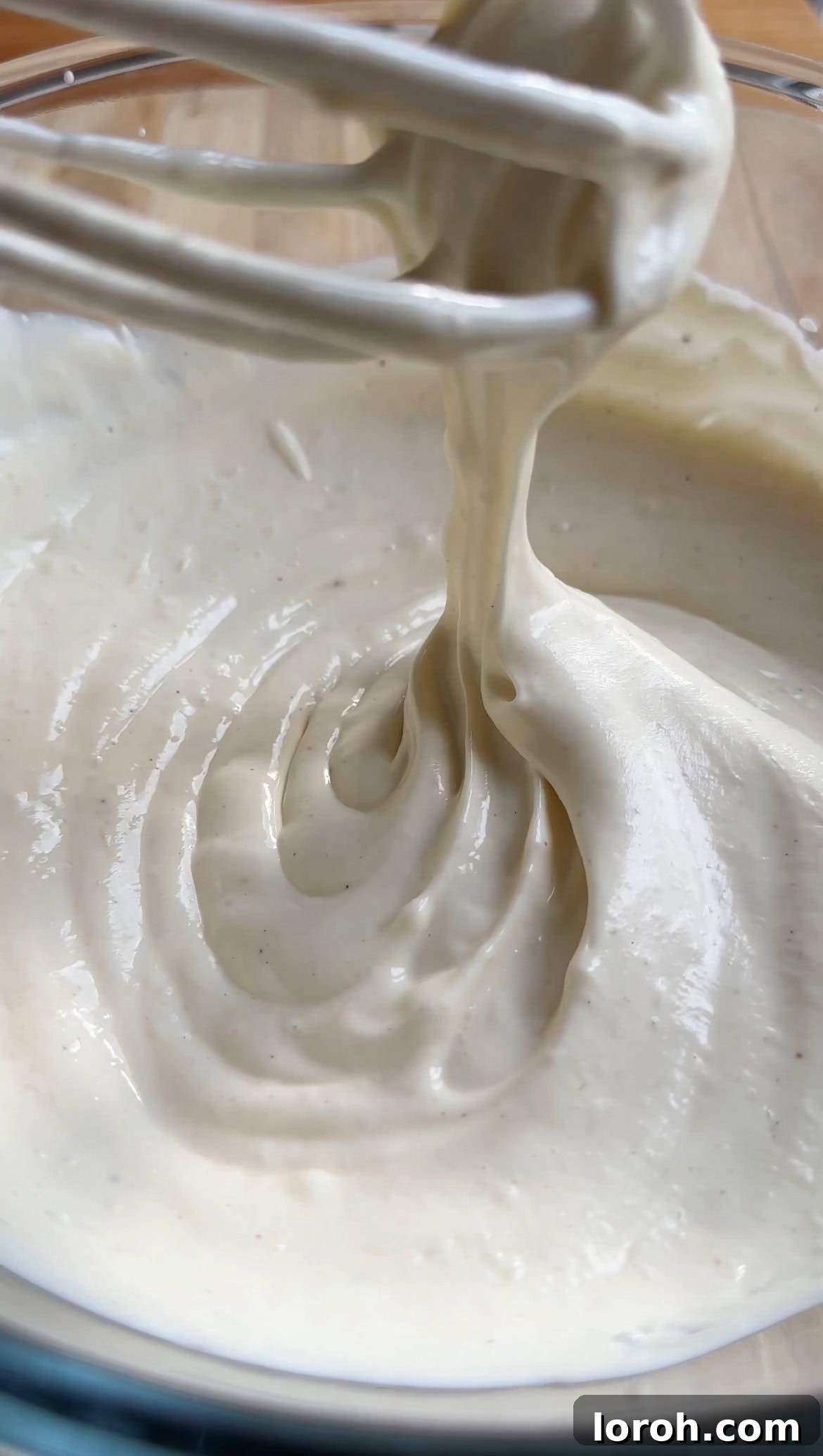 Blending the cream cheese, icing sugar, and vanilla extract with an electric whisk until the mixture is smooth and lump-free, forming the cheesecake base.
