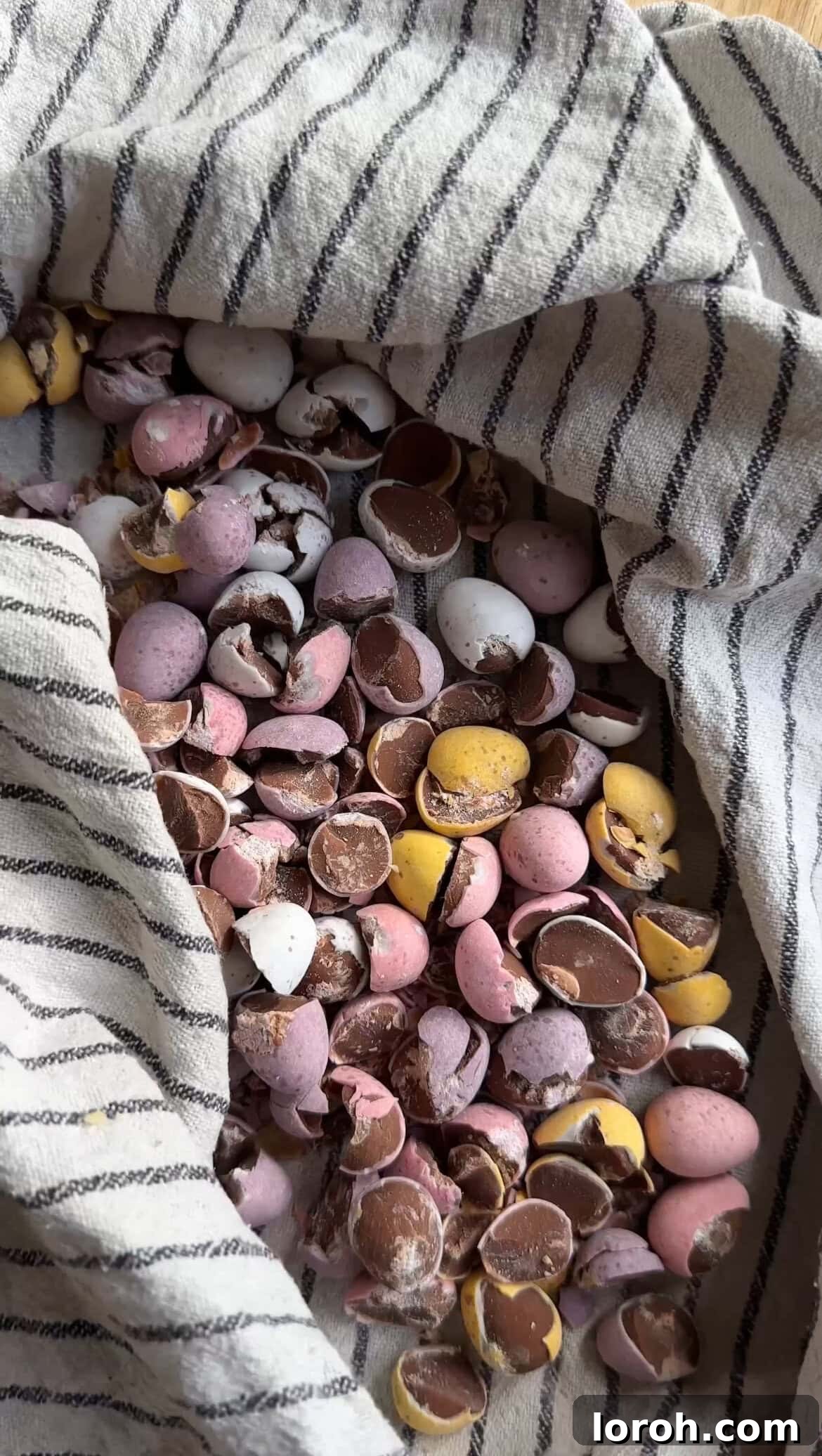 Crushing Mini Eggs inside a tea towel with a rolling pin, creating a mix of chunks and smaller pieces for texture in the cheesecake.