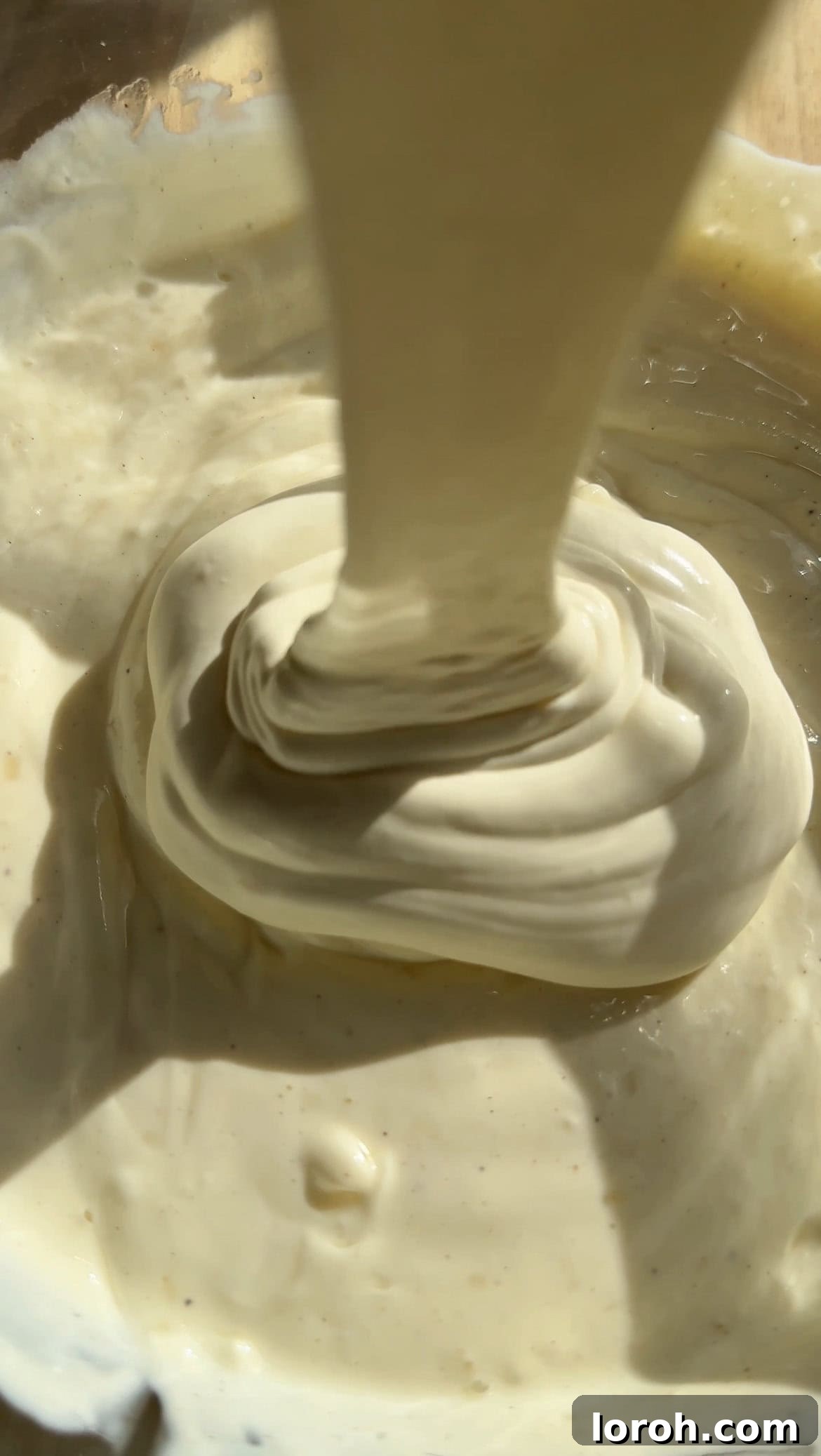 Pouring cold double cream into the smooth cream cheese mixture, ready for whisking to create a thick cheesecake filling.