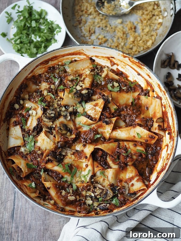 Lentil and mushroom bolognese in a shallow white casserole dish, served with pasta and fresh parsley, showcasing its rich texture and vibrant colors.