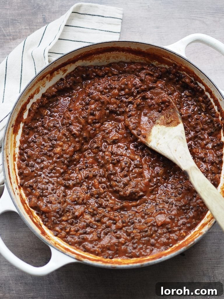 The rich lentil bolognese sauce, made with passata, vegetable stock, and seasonings, gently simmering in a shallow casserole dish, creating a luscious texture and melding flavors.