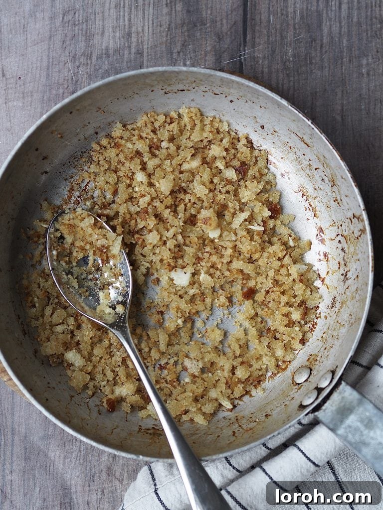 Fresh breadcrumbs being toasted to a beautiful golden crisp in a metal frying pan with a little olive oil, creating the essential pangrattato topping.