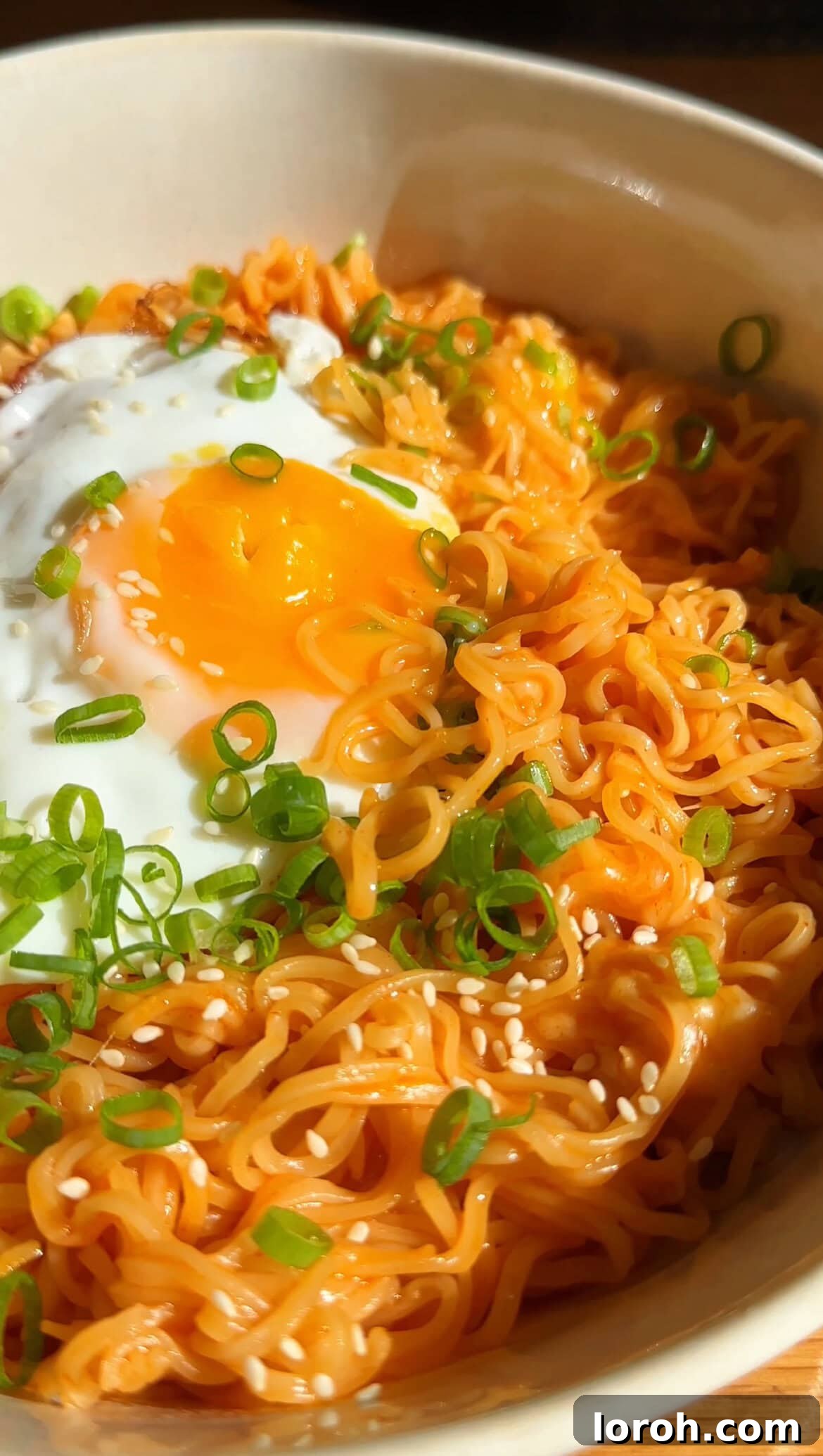 Korean Fire Cheese Noodles 3 A close-up of cheesy Korean Spicy Ramen Noodles, garnished with fresh spring onions and a golden-fried egg, showcasing the rich texture.