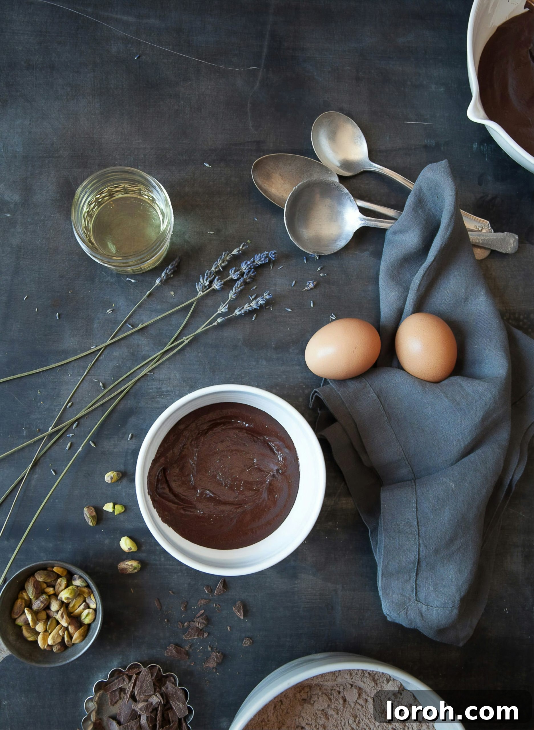 Baking ingredients laid out on a dark background with eggs and a bowl of melted chocolate.