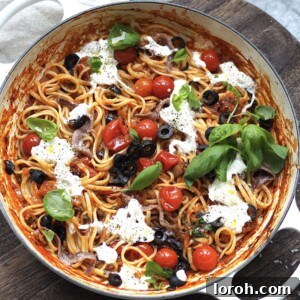 White shallow casserole with puttanesca dotted with torn burrata and fresh basil.