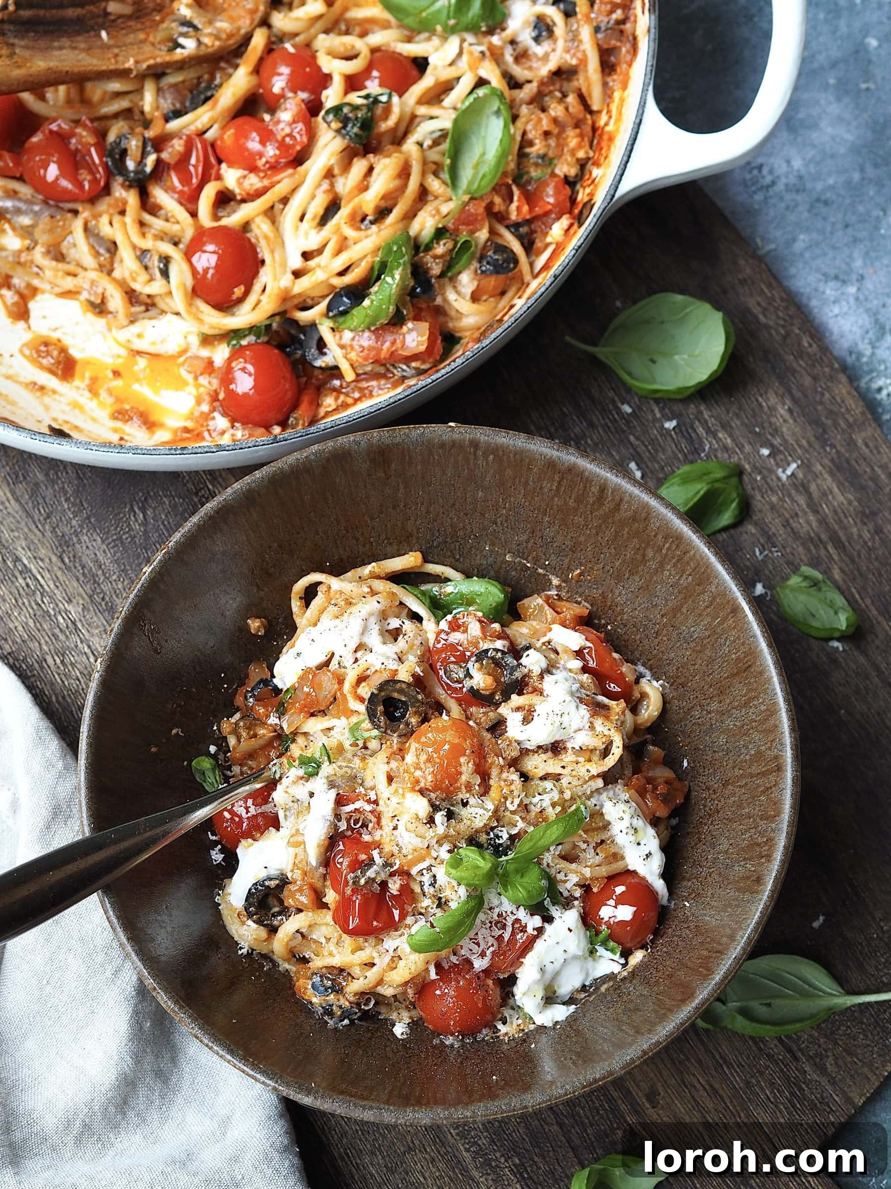 Bold Penne Puttanesca 3 Bowl of pasta with burrata, cherry tomatoes and black olives topped with fresh basil next to the casserole dish filled with pasta, showcasing the final dish.