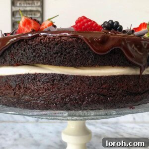 Side angle of moist chocolate cake filled with cream and topped with berries and ganache