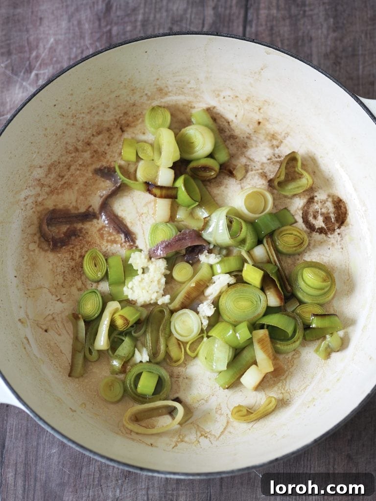 Velvety Caramelized Leek & Gruyère Pasta 7 Garlic being added to slow cooked leeks in a shallow casserole.