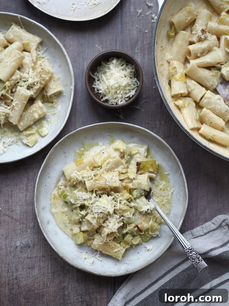 Velvety Caramelized Leek & Gruyère Pasta 10 Plate of creamy leek pasta next to the shallow casserole of cooked pasta and a small bowl of grated cheese.