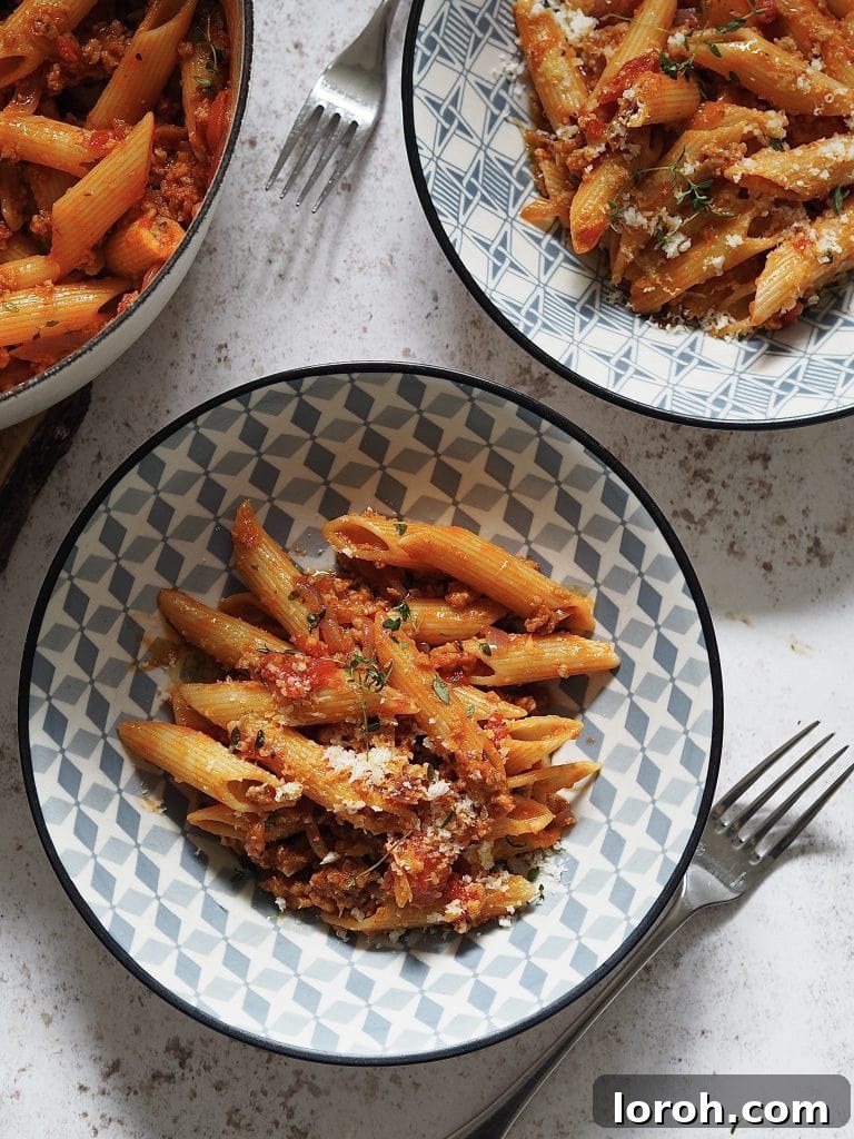 Hearty Weeknight Sausage Ragu 2 A vibrant blue and white bowl filled with penne pasta and rich Weeknight Sausage Ragu, topped with fresh herbs and grated cheese.