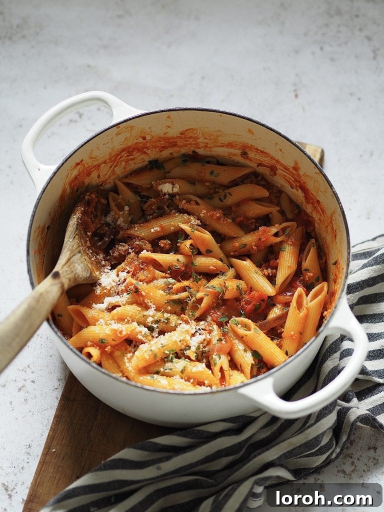 Hearty Weeknight Sausage Ragu 3 A wooden spoon stirring a generous portion of creamy tomato and sausage ragu in a white casserole dish, showcasing its rich texture.
